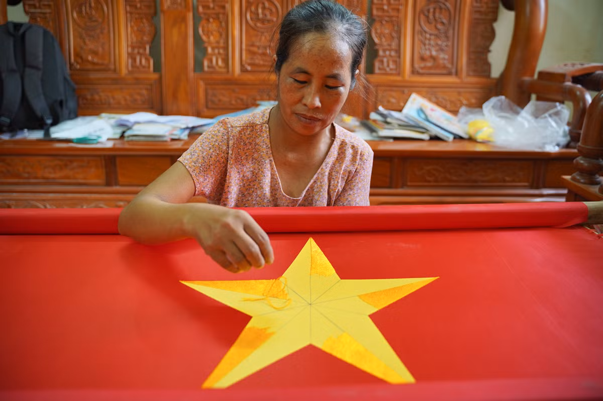 Cô Nguyễn Thị Huấn miệt mài thêu cờ Tổ quốc. "Thêu một lá cờ bằng tay là cả một quá trình tỉ mỉ, thường kéo dài từ 2-3 ngày. Với những người mới bước vào nghề, thời gian hoàn thành có thể lên đến cả tuần lễ. Mỗi đường kim, mũi chỉ được thêu lên lá cờ đều đòi hỏi sự chính xác tuyệt đối", cô Huấn nói.