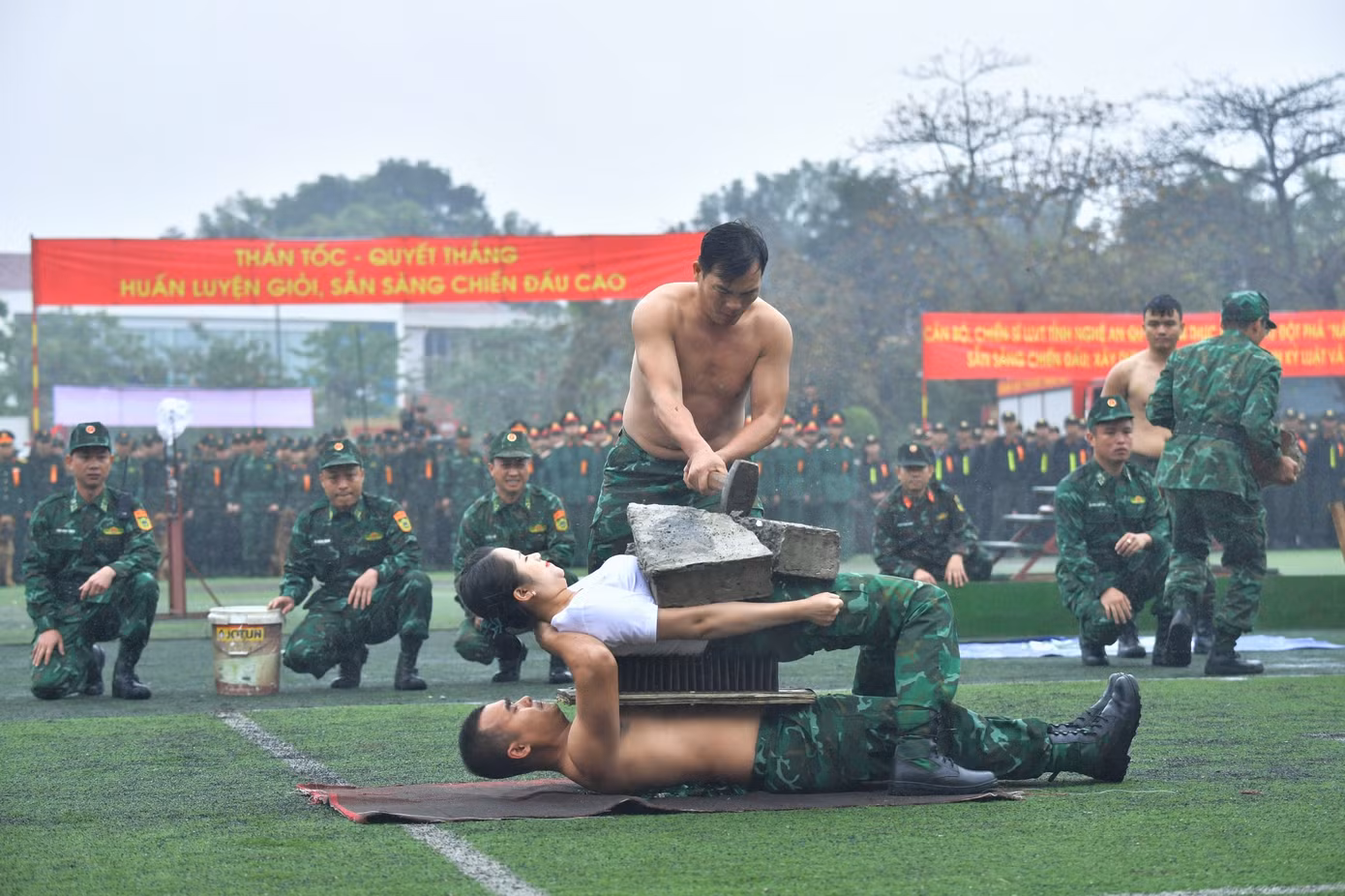 Hai cán bộ Biên phòng nằm trên thủy tinh vỡ, trên bàn chông để đồng đội dùng búa tạ đập vỡ tảng đá trên người.