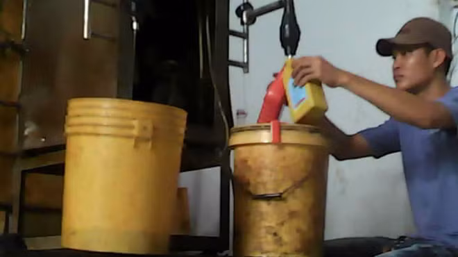 Người làm tại Công ty Vạn Thành đổ nhớt tái chế đã được pha hóa chất vào các chai mang nhãn hiệu khác nhau rồi đóng nắp thành sản phẩm hoàn chỉnh - Ảnh từ clip