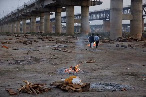 Một gia đình đứng gần một giàn thiêu, nơi thiêu người nhà của họ, tại một khu hỏa táng ở Prayagraj. Ảnh: AP.