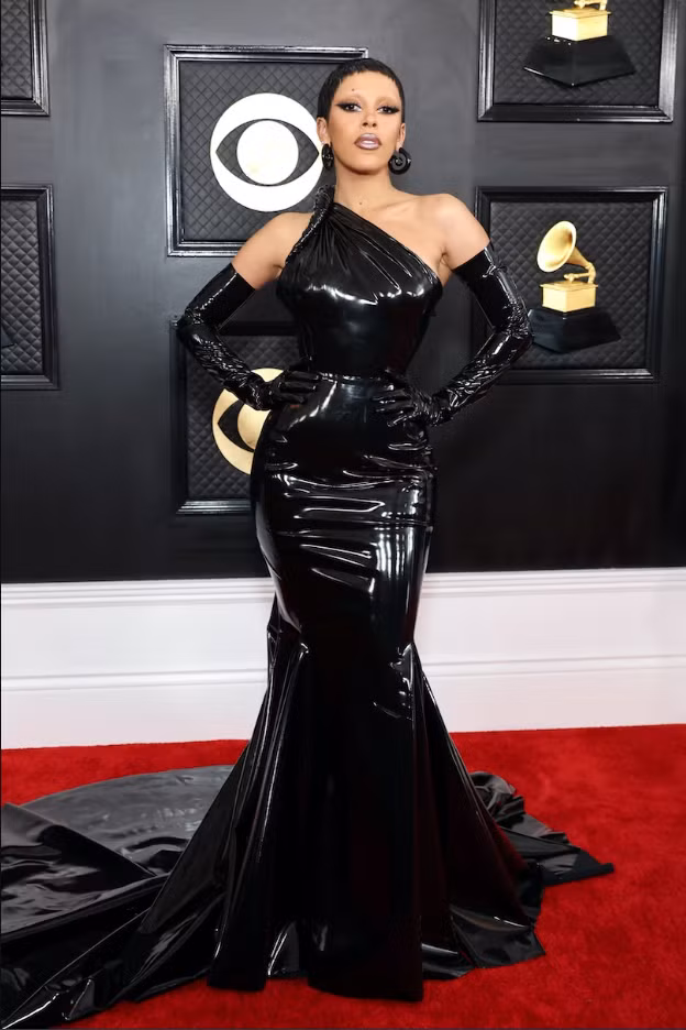 Kiểu tóc pixie cắt sát của Doja Cat, hoa tai đen nổi bật, áo choàng Atelier Versace xếp li màu đen và găng tay dài opera gợi nhớ đến phù thủy Ursula (phim Nàng tiên cá).