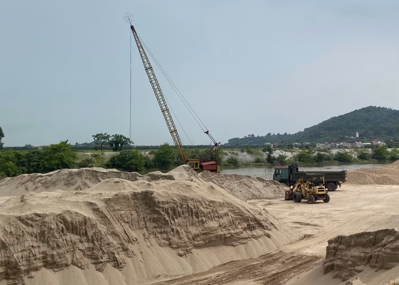 Các núi cát khổng lồ được chất cao cả chục mét nằm ngay sát bờ sông.