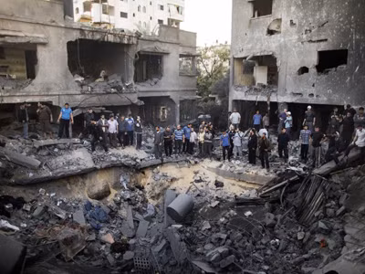 Người dân Palestine đứng quanh hố bom xuất hiện sau đợt không kích của Israel vào thành phố Gaza hôm 18-11