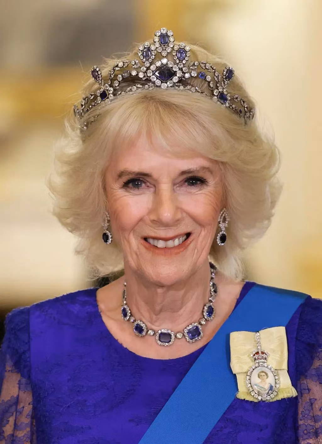 Hoàng hậu Camilla nhận được sự chú ý lớn khi đội vương miện Belgian Sapphire Tiara yêu thích của mẹ chồng, cố Nữ hoàng Elizabeth II. Bà kết hợp với chiếc váy ren màu xanh hoàng gia do Bruce Oldfield thiết kế, cùng với bông tay và vòng cổ phù hợp với vương miện, tạo nên vẻ ngoài quý phái, vương giả. Ảnh: Getty Images.