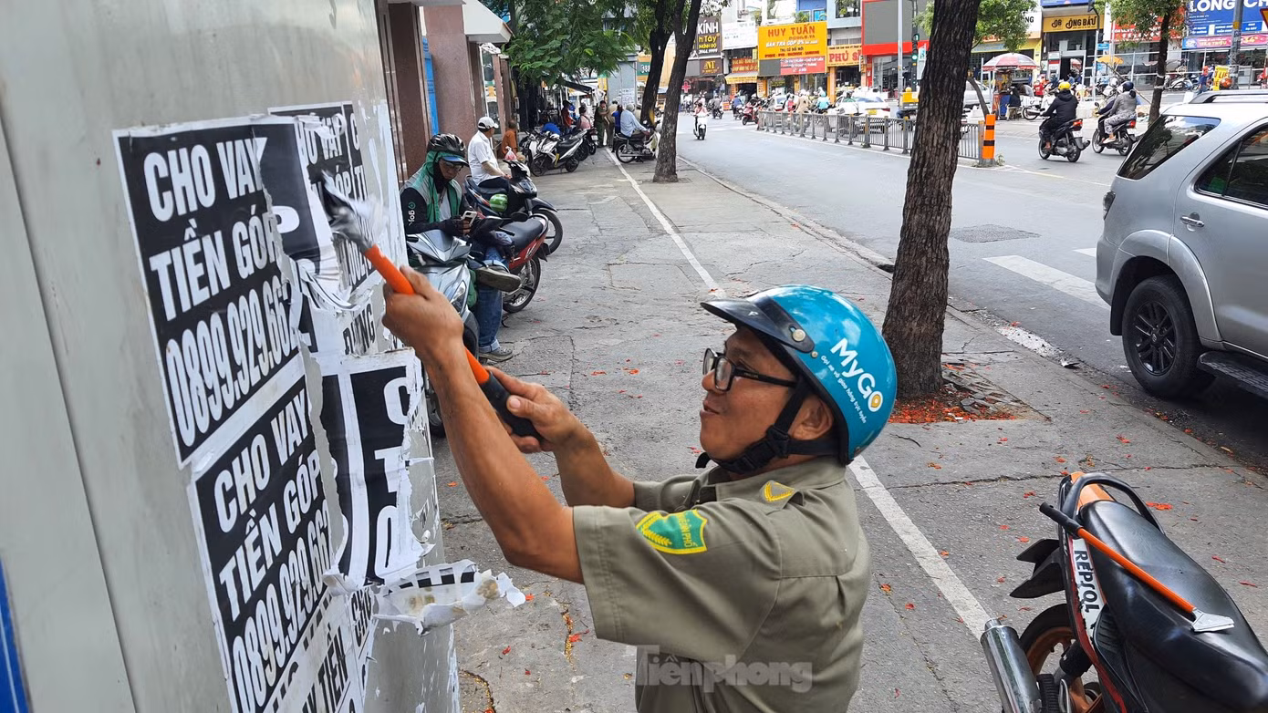 Lực lượng bảo vệ dân phố bóc, gỡ tờ rơi quảng cáo cho vay tiền dán trên tủ điện. Ảnh: Hoàng Thuận.