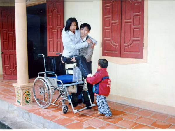 Anh Chín bế chị Phương lên xe lăn