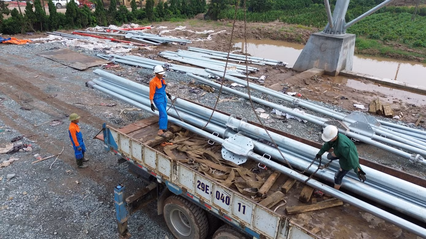 Bên dưới, nhóm công nhân phân loại các thanh, cột, chuẩn bị vật tư trước khi buộc vào dây tời để kéo lên.