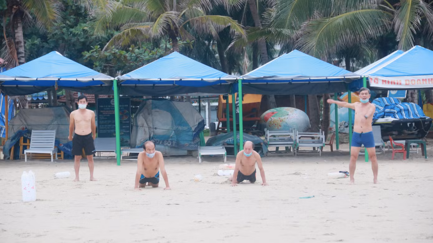 Một nhóm người lớn tuổi tập thể dục, khởi động tay chân trước khi xuống biển. Mọi người đều giữ khoảng cách theo quy định.