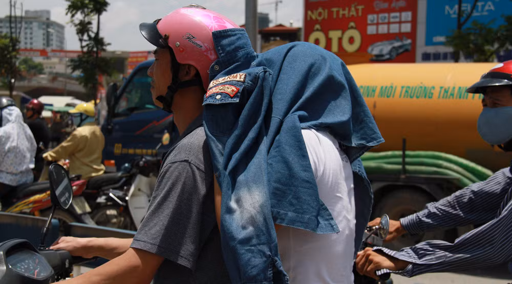 Một phụ nữ lấy áo che đầu trong khi chờ đèn đỏ. Ảnh: Trường Phong