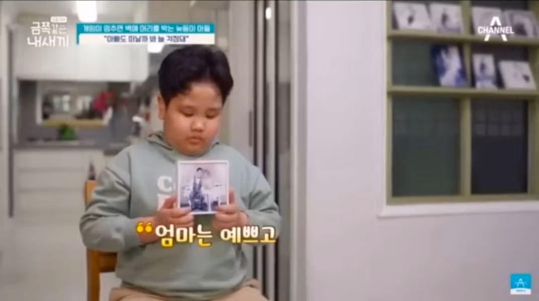 Cậu bé cầm lấy bức ảnh chụp của ba và mẹ, ngậm ngùi kể về người mẹ đã mất của mình. Cậu bé cầm lấy bức ảnh chụp của ba và mẹ, ngậm ngùi kể về người mẹ đã mất của mình.