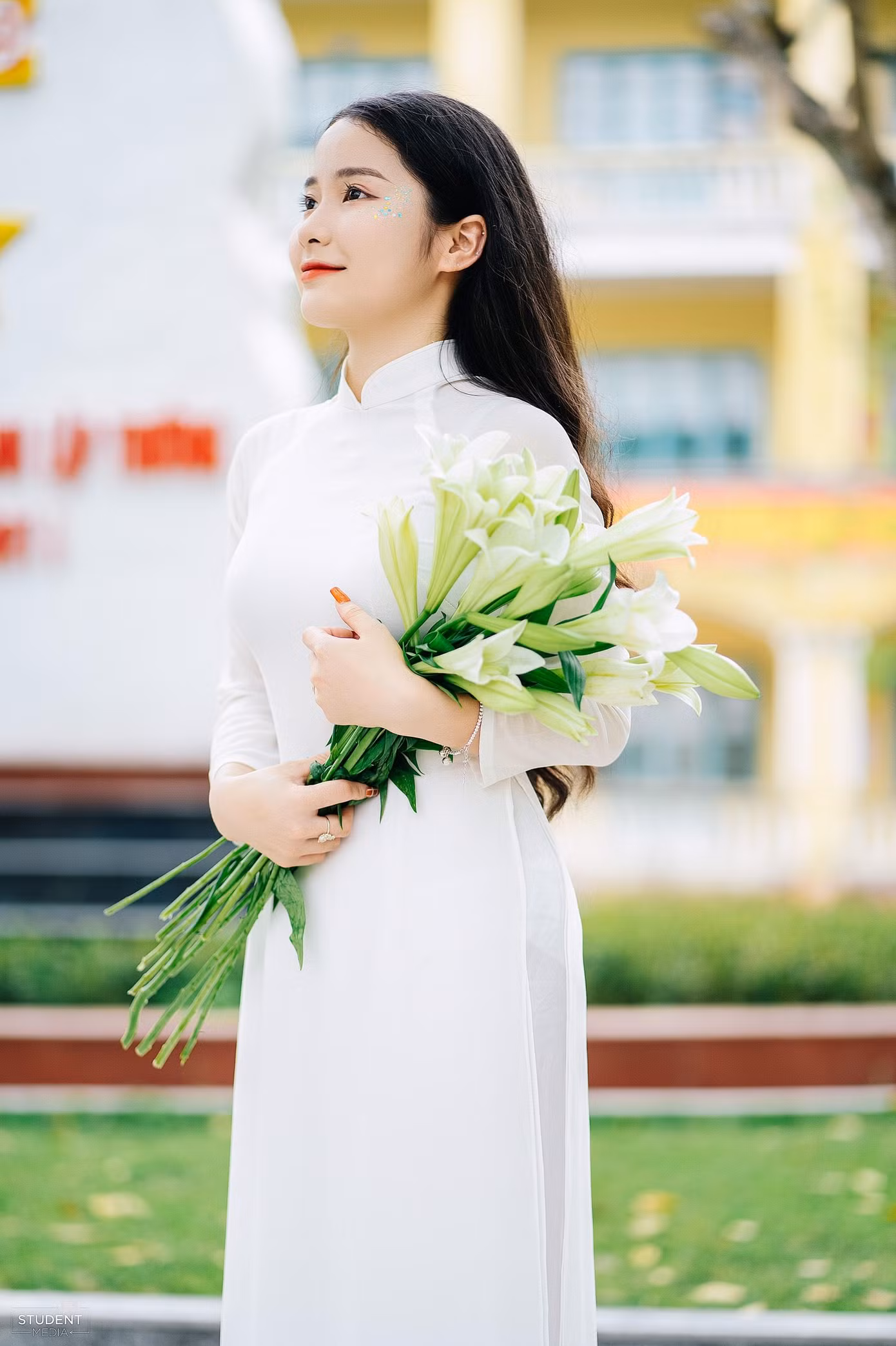 Huyền Trang chụp ảnh kỷ yếu với áo dài trắng và hoa huệ tây.