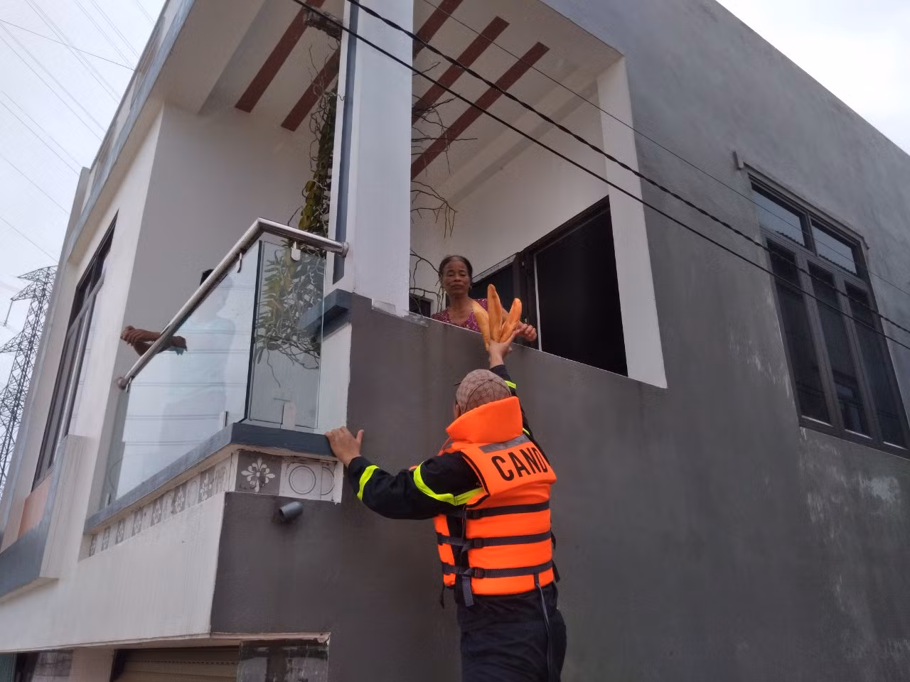 Công an đưa bánh mì ăn sáng cho người dân ở trên tầng 2. Hiện trong thôn Đa Hội, nhiều người dân vẫn ở trên tầng 2 hoặc tầng 3 của nhà mình mà chưa muốn di chuyển ra bên ngoài. Ảnh: Nguyễn Thắng