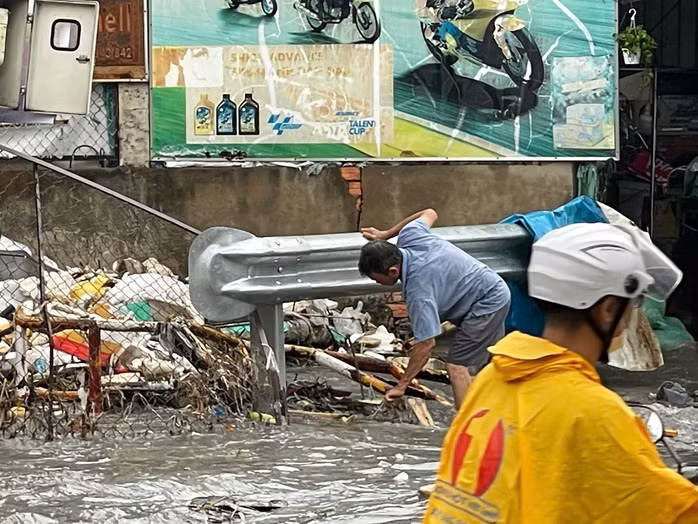 Người dân vớt rác khỏi miệng cống thoát nước.