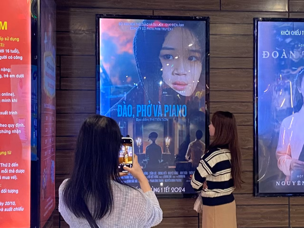 Khán giả trẻ chụp ảnh cùng poster phim Đào, phở và piano tại Trung tâm chiếu phim Quốc gia, tối ngày 22/2.