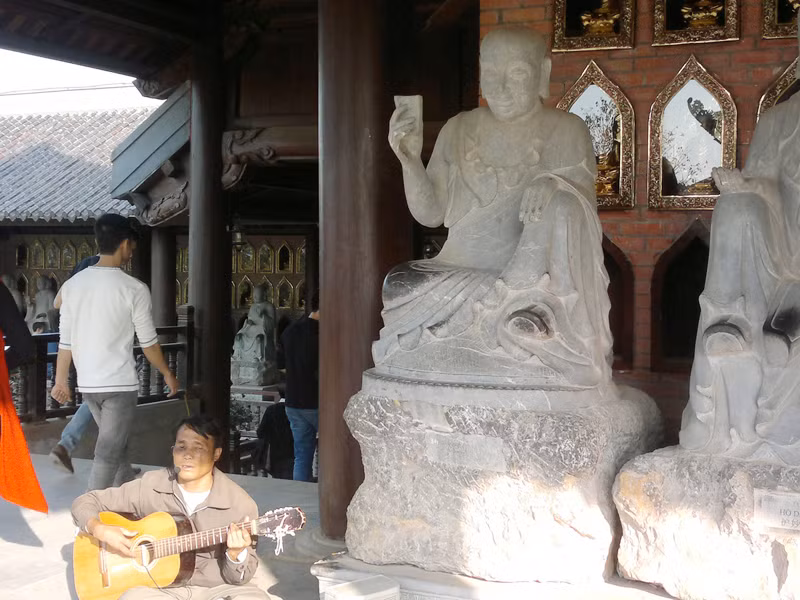 Người đàn ông mù lòa chơi bản đàn buồn bã và hát những lời ai oán về đời mình ngay cạnh những bức tượng La Hán (chụp tại chùa Bái Đính mới). Người đàn ông mù lòa chơi bản đàn buồn bã và hát những lời ai oán về đời mình ngay cạnh những bức tượng La Hán (chụp tại chùa Bái Đính mới)
