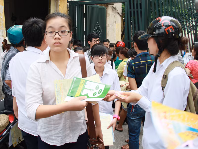 Những nhân viên phát tờ rơi xếp hàng ngay ngoài cổng trường, phát cả tập tờ rơi đến từng thí sinh. Ảnh: Trường Phong