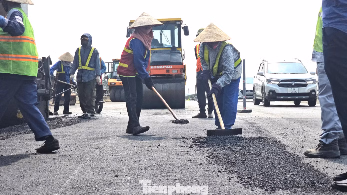 Công nhân dùng các dụng cụ thủ công để tinh chỉnh các điểm máy rải nhựa chưa đều để tránh dằn xóc.