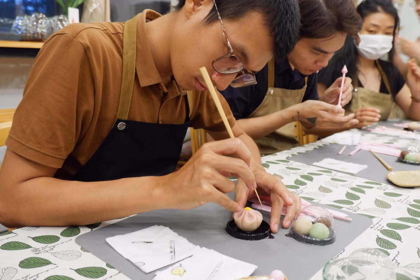 Khải đang hướng dẫn các bạn trẻ trong một workshop làm bánh. Khải đang hướng dẫn các bạn trẻ trong một workshop làm bánh.