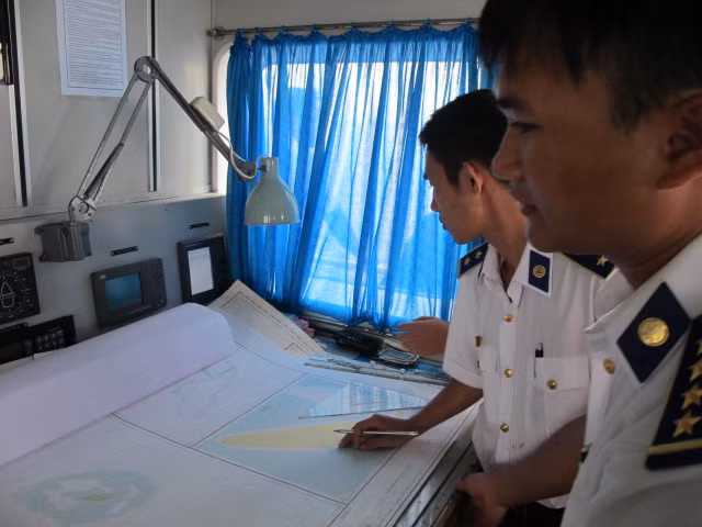 Thuyền trưởng Phạm Nguyên Phú (bên phải) đang cùng đồng đội xem bản đồ, tính toán độ nông sâu của khu vực có tàu cá lạ.