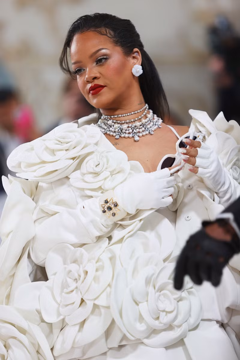 Rihanna xuất hiện trong một chiếc váy trắng cùng tấm áo khoác khổng lồ với 30 bông hoa làm từ 500 cánh hoa trà.