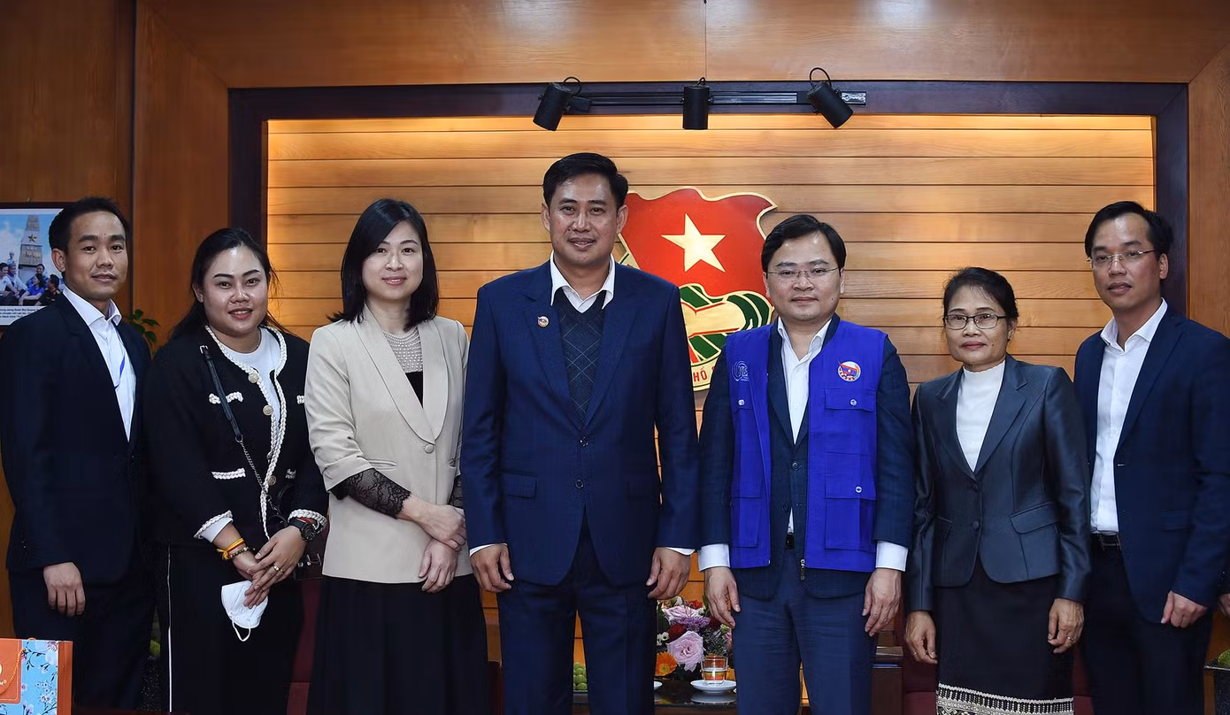Các đại biểu chụp ảnh lưu niệm. Anh A Lun Xay Sủn Nạ Lạt tặng anh Nguyễn Anh Tuấn chiếc áo xanh của thanh niên tình nguyện Lào tham gia phòng chống dịch COVID-19. Ảnh: Xuân Tùng.