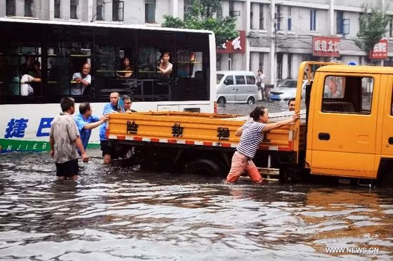 Mọi người di chuyển một chiếc xe ra khỏi đoạn đường ngập nước ở quận Thiết Tây, Thẩm Dương, thủ phủ tỉnh Liêu Ninh, đông bắc Trung Quốc, ngày 16/8/2013. Ảnh: Tân Hoa Xã 