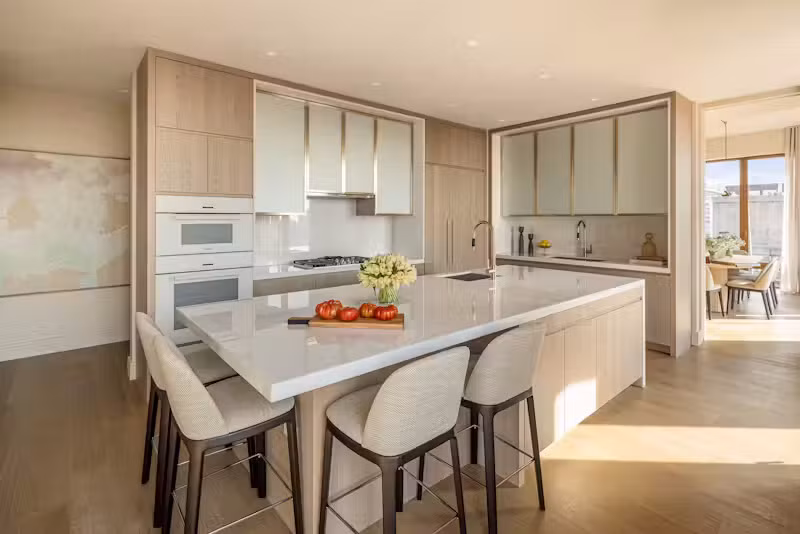 Bếp ăn cao cấp được thiết kế như một không gian nghệ thuật với cửa sổ kính lớn hướng Bắc, đảo bếp cỡ lớn cùng hệ tủ gỗ tần bì nhuộm màu riêng biệt, nổi bật với tủ kính gợn sóng phía trên và mặt bếp cùng tường ốp bằng đá cẩm thạch Bianco Ice sáng bóng.