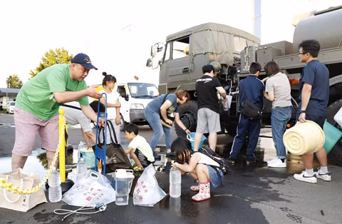 Một số người tranh thủ hứng nước từ các xe bồn ở thị trấn Atsuma. Ảnh: REUTERS.