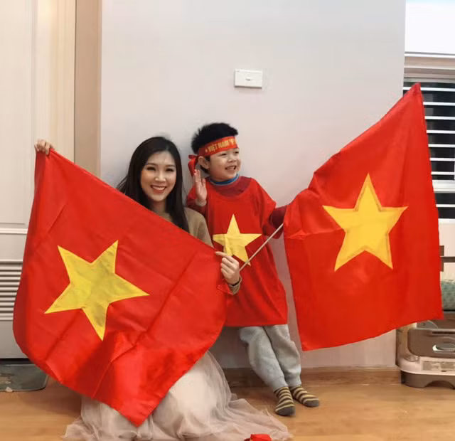 Mẹ con Hoa hậu Áo dài Phí Thuỳ Linh mặc áo cờ đỏ sao vàng, giơ cờ Tổ quốc cổ vũ cho đội nhà.