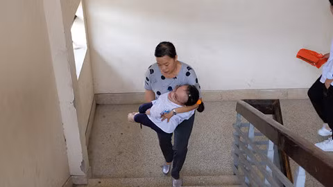 Hoài Thương được mẹ bế lên tầng 4 để làm vào phòng thi. ẢNH:LÃ NGHĨA HIẾU.