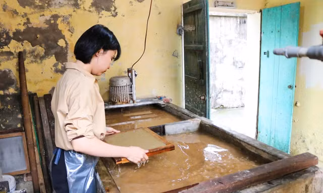 Giữa xưởng nhỏ thoang thoảng mùi vỏ dó, đôi tay chị Huyền miệt mài bên bể bột, thoăn thoắt xeo từng tờ giấy mỏng nhẹ.